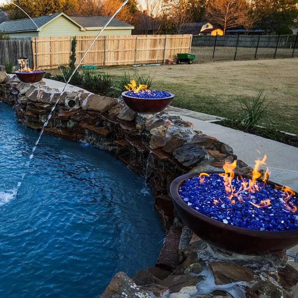 Fire pit with blue glass stones by a pool in a backyard setting
