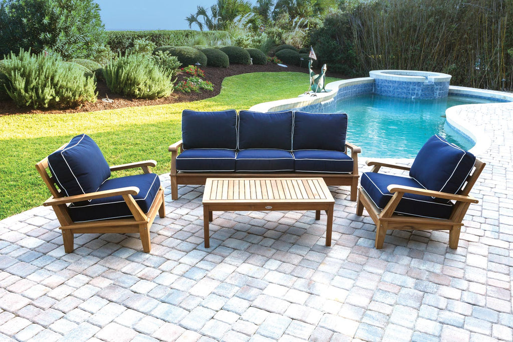 Teak outdoor sofa with dark blue cushions and three back pillows, angled view