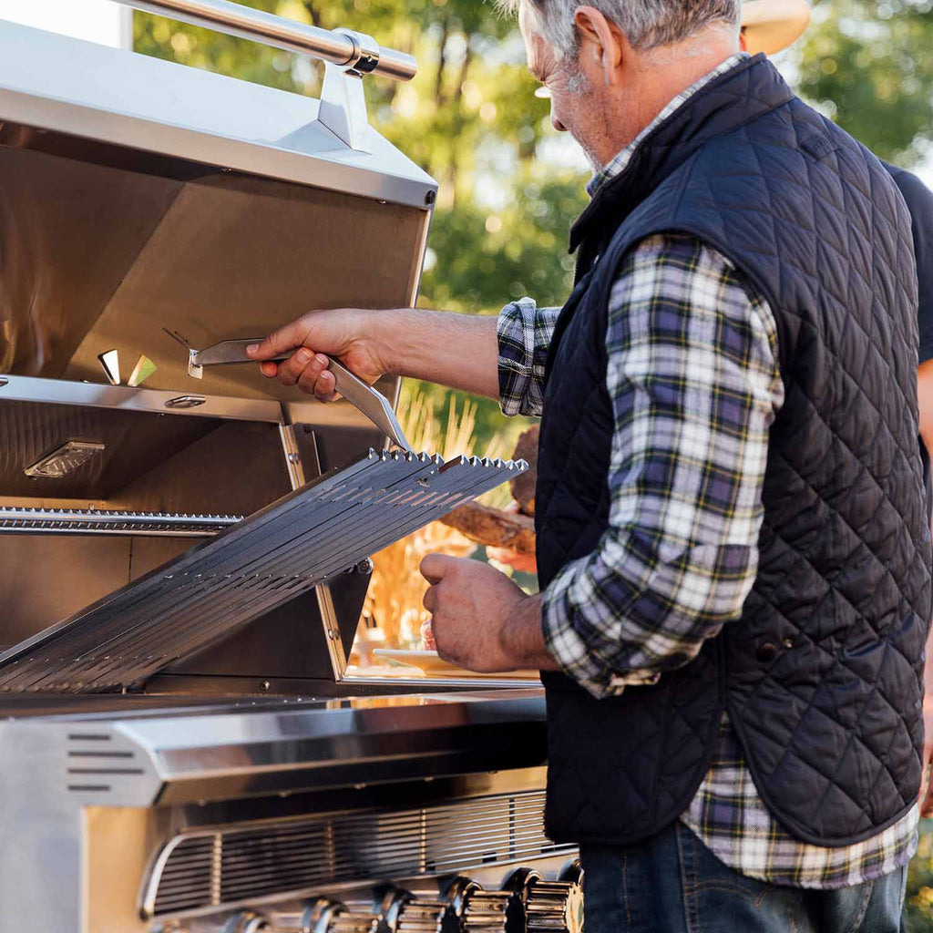 Person grilling with the lid open, placing food on the cooking grate on the cart.