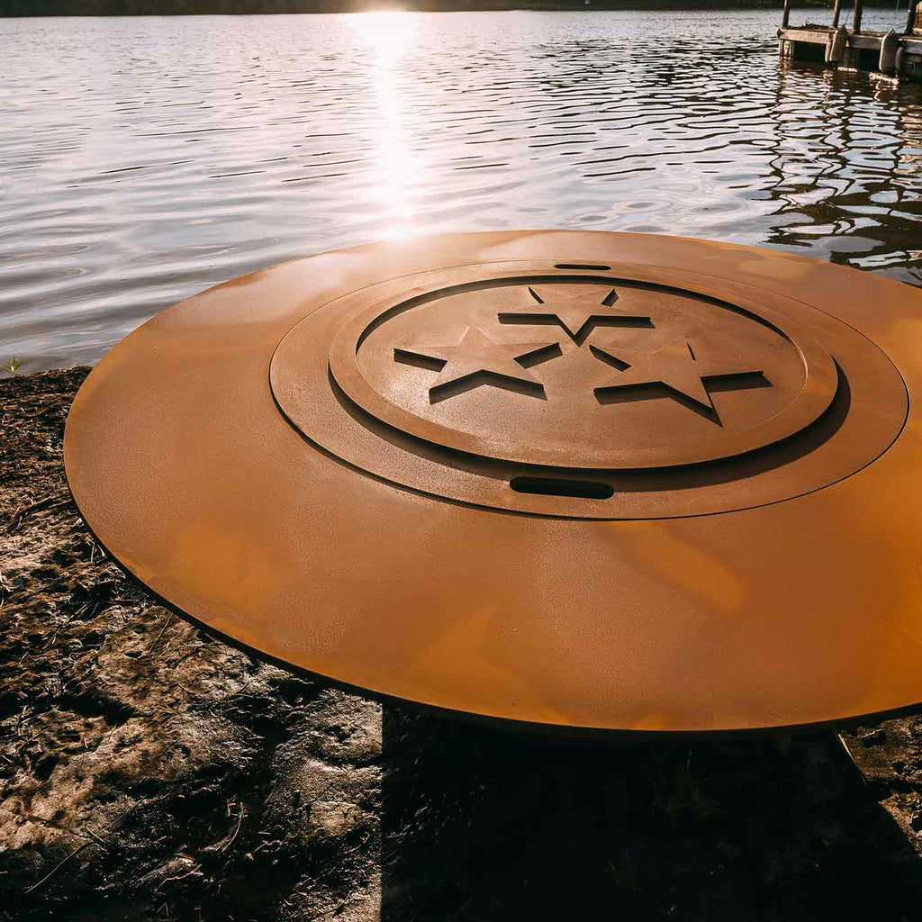 Round gas fire pit lid with star-shaped burner cutout on outdoor stone