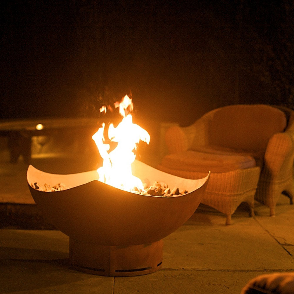 Manta ray gas fire pit with orange-brown bowl and flames in outdoor seating area