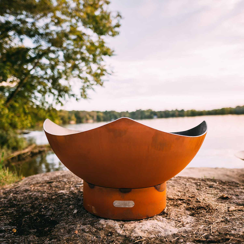 Orange-brown manta ray gas fire pit with dark inner bowl on outdoor ground