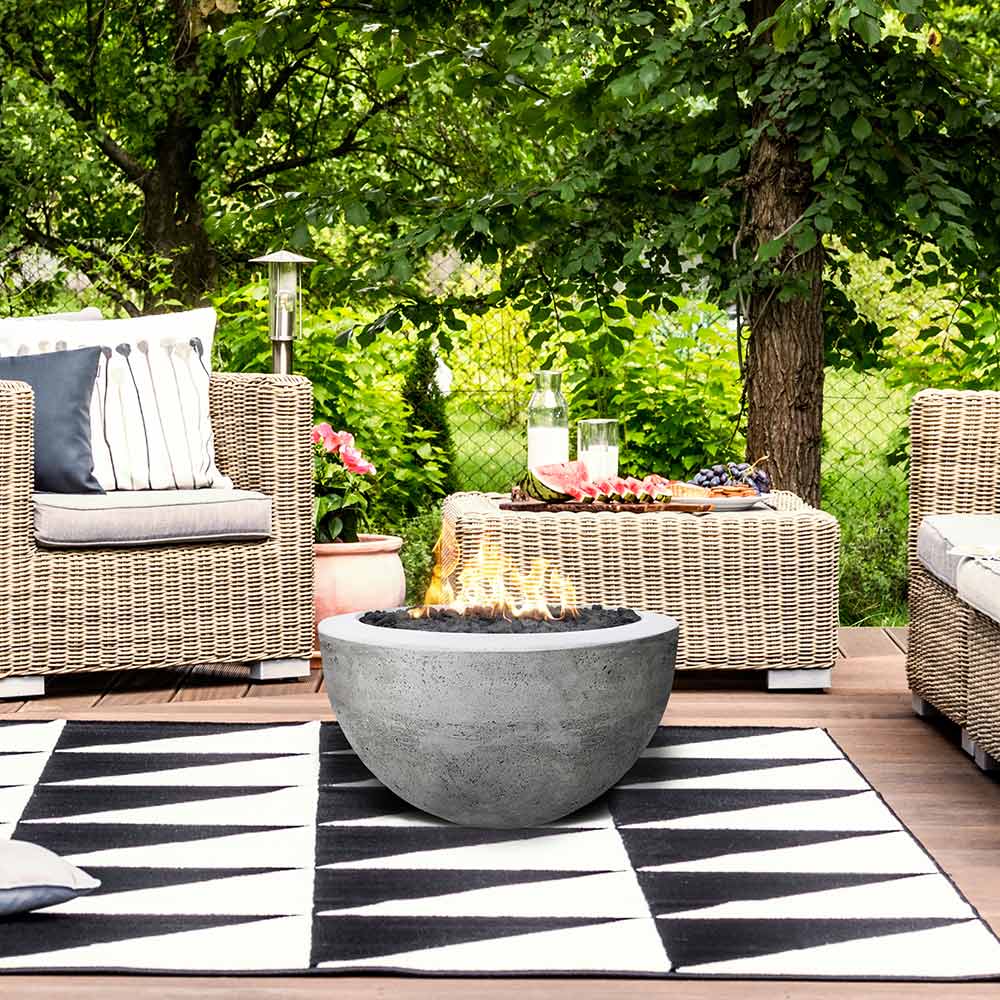 Concrete gas fire pit bowl in light gray with burner opening, centered on rug