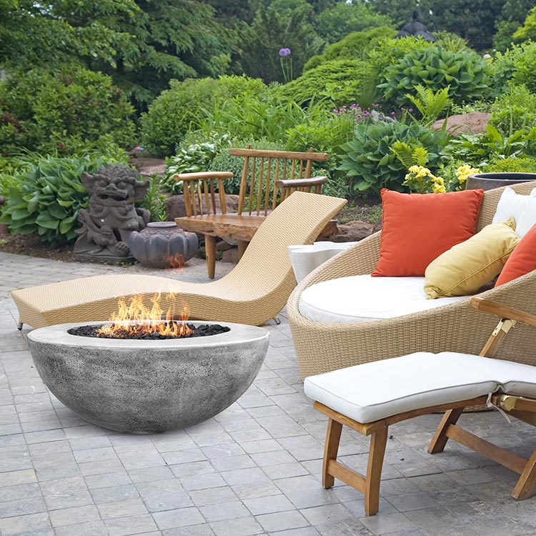 Concrete gas fire pit with flames on patio stones, near outdoor seating