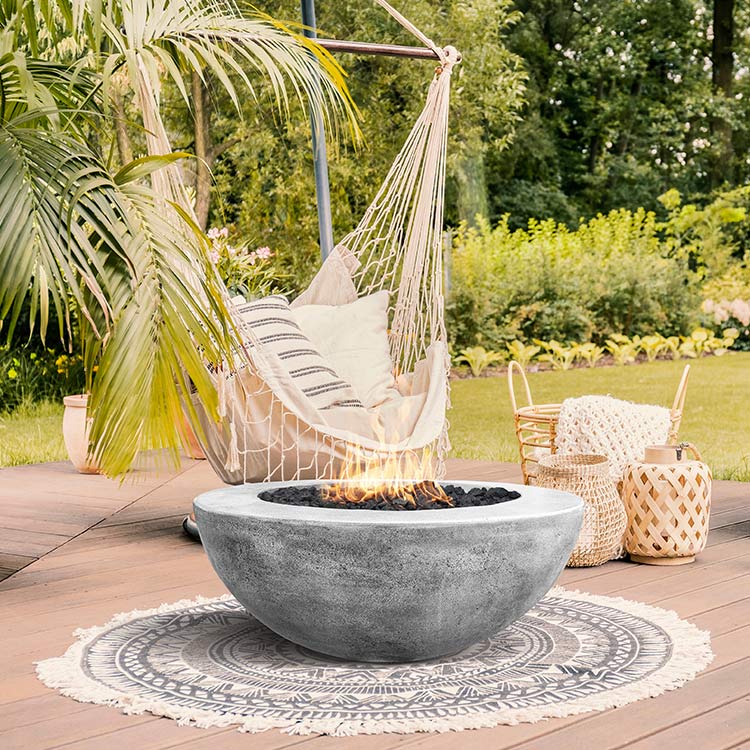 Concrete gas fire pit with flames on a patio, beneath a hanging hammock
