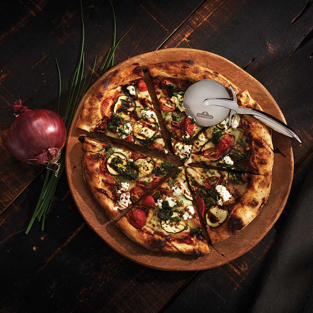 Pizza wheel resting on a vegetable pizza with sliced toppings