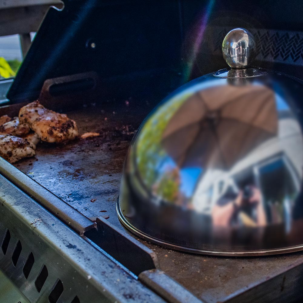 Stainless steel cooking dome with knob covering a grilling surface
