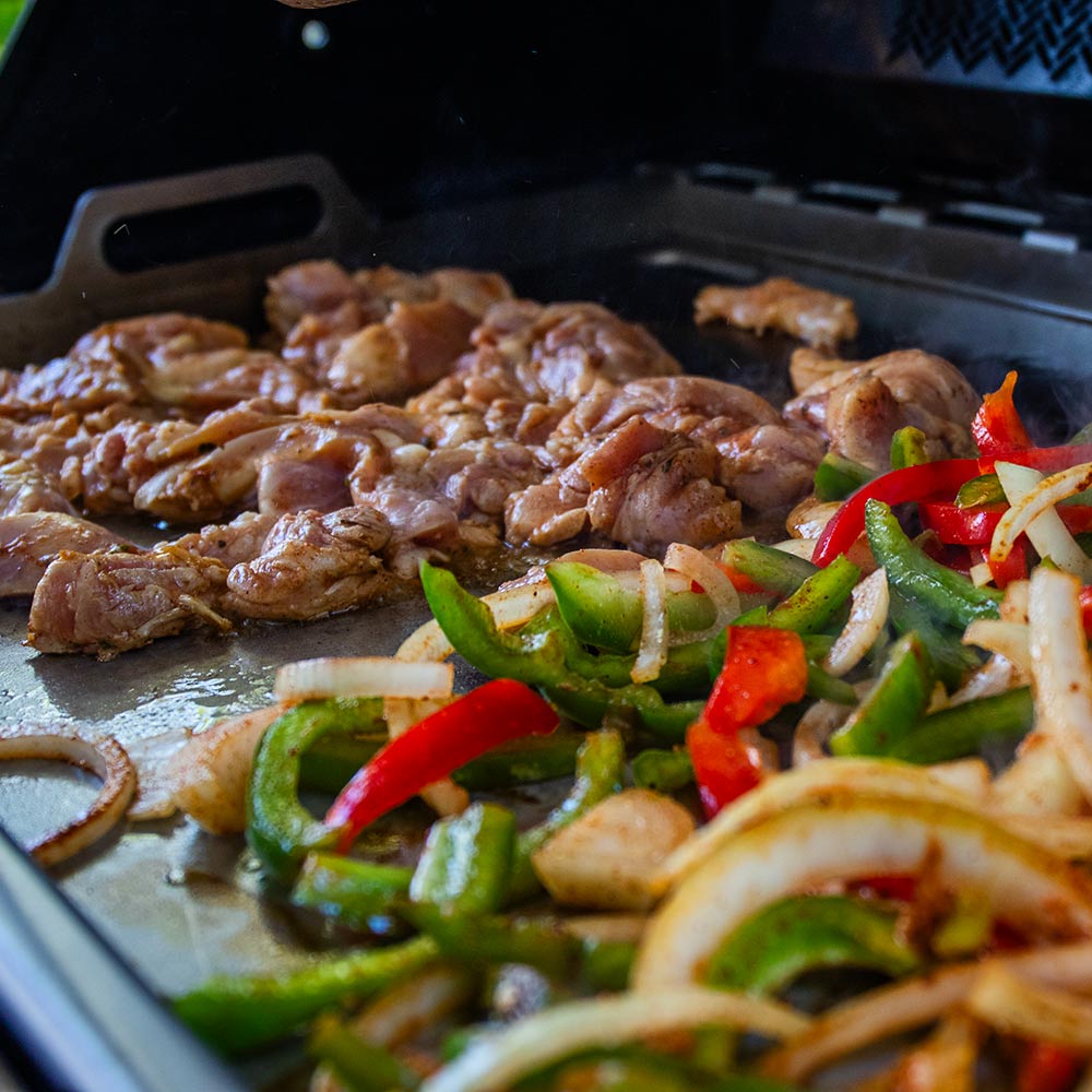 Stainless steel griddle insert cooking surface with sizzling meat and vegetables