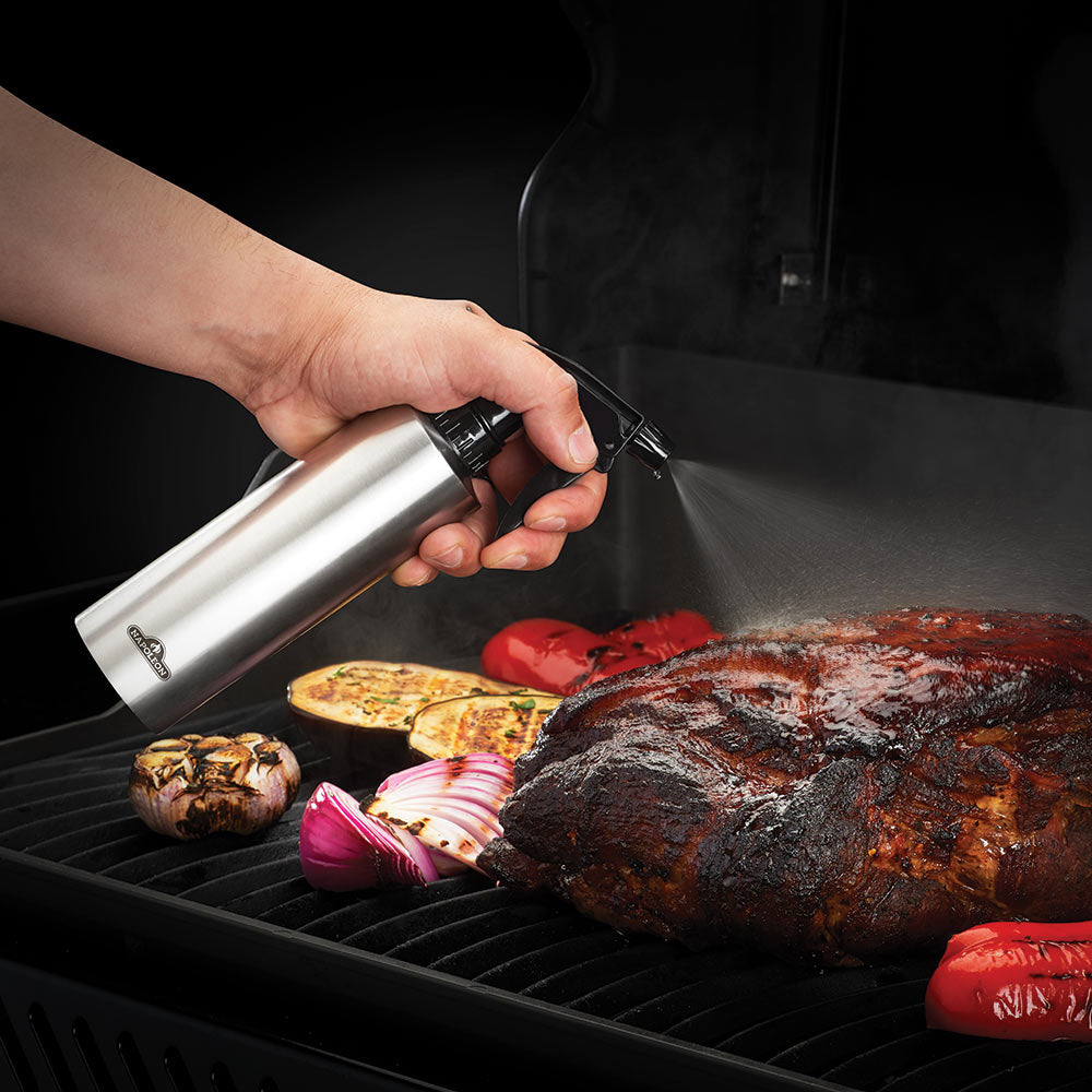Stainless steel spray bottle with black trigger in hand, misting grilled food