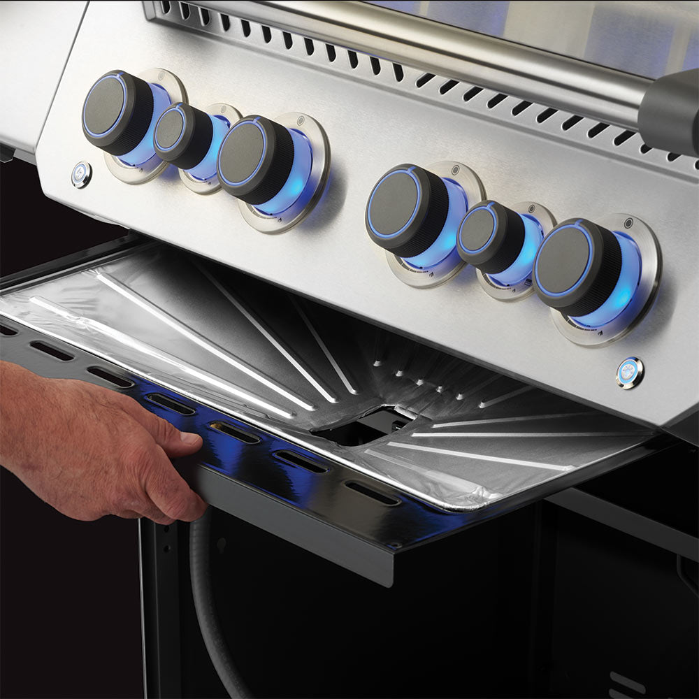 Grill drip pan liner being placed in grill firebox, foil sheet covering tray