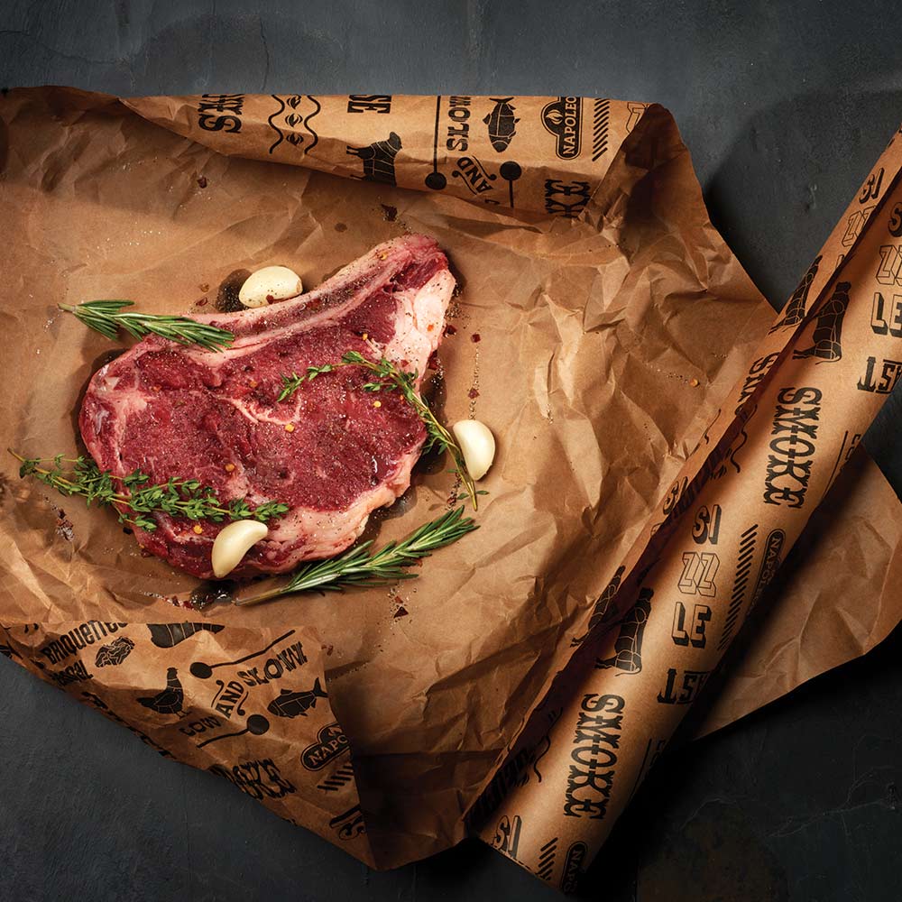 Butcher paper sheet holding raw meat with herbs and garlic visible