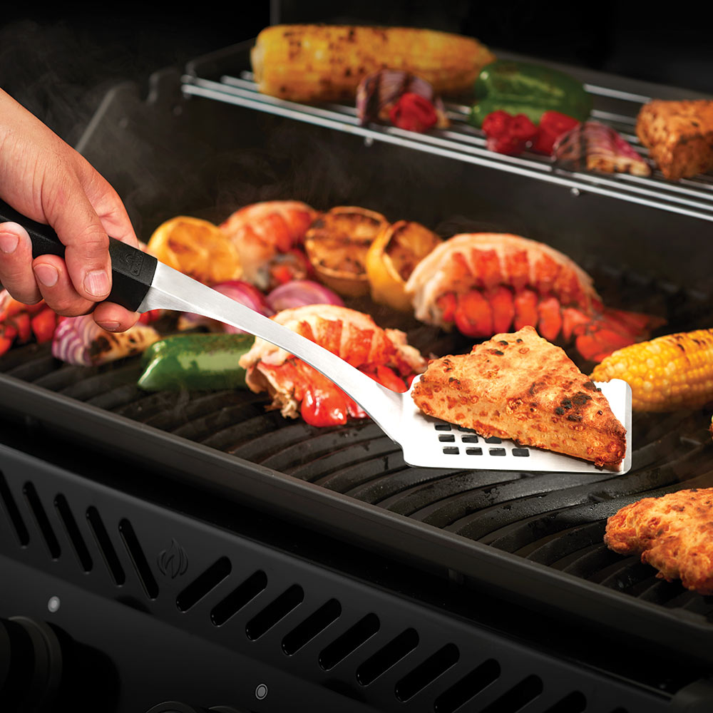 BBQ spatula lifting grilled meat and vegetables on metal grill