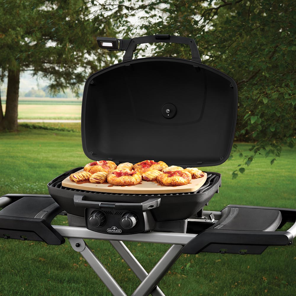 Beige pizza stone on open grill with round baked items