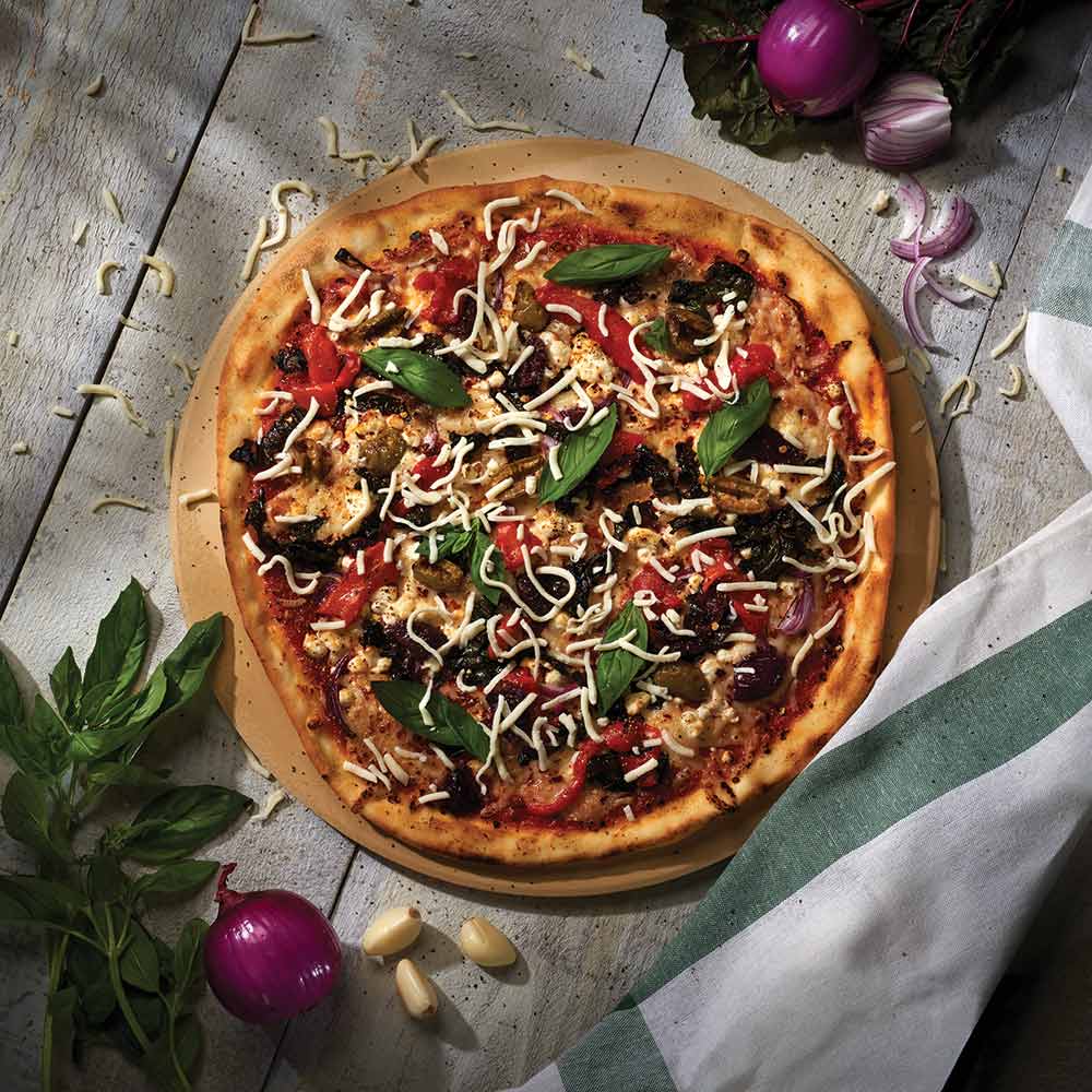 Pizza on round pizza stone with toppings and shredded cheese