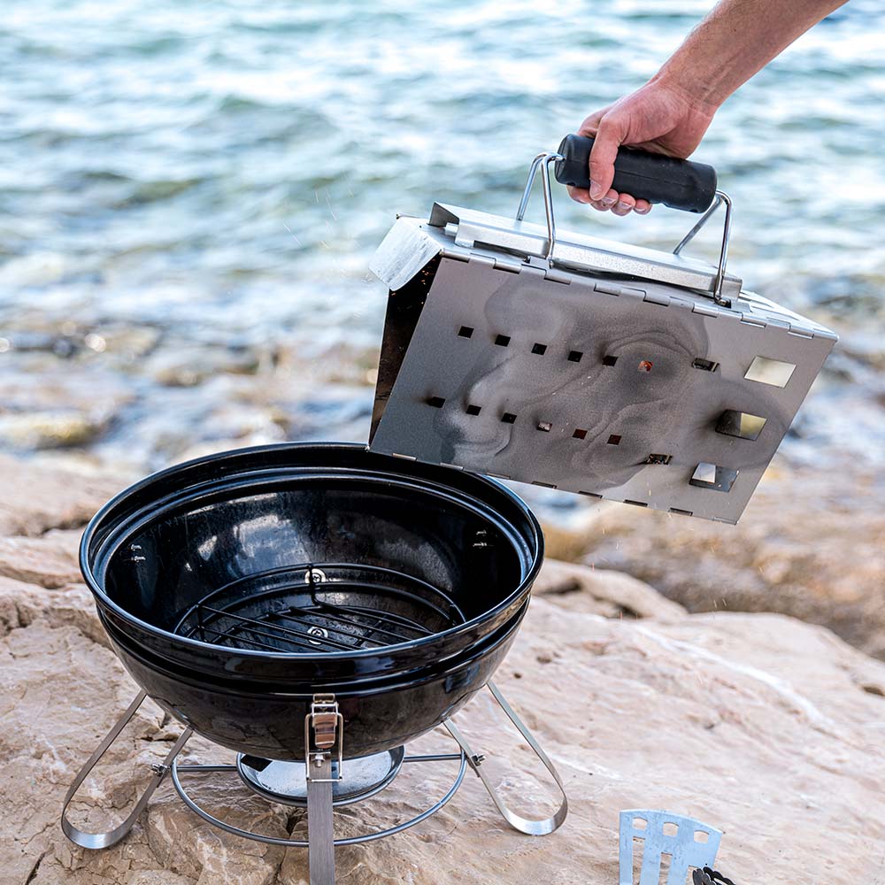 Portable charcoal kettle grill on stand with lid open and circular cooking grate
