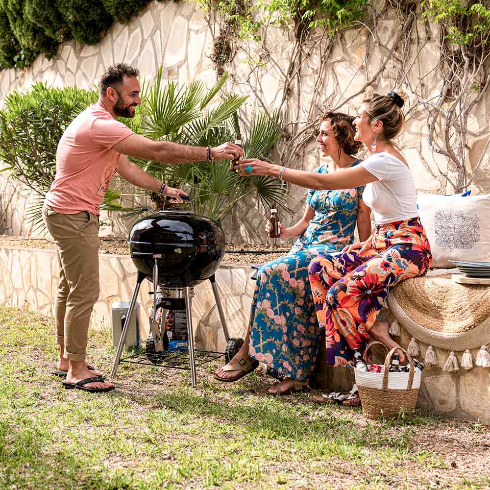 Outdoor charcoal kettle grill with domed lid and chrome cooking grate on three legs