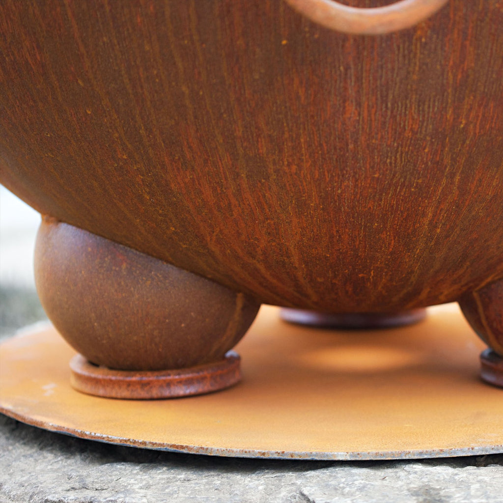 Fire pit base plate with rusted metal disc and rounded legs, underside view.