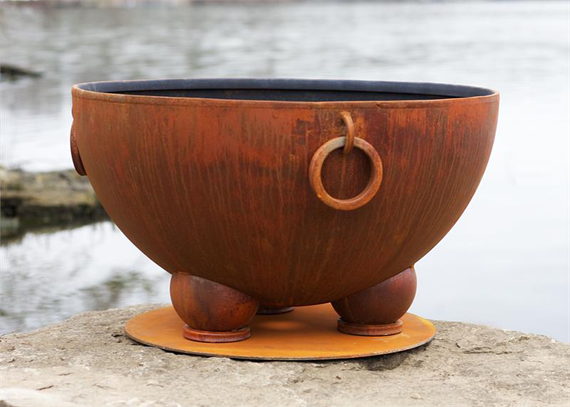 Wood fire pit bowl on a round base, circular side handle detail, copper-brown metal.