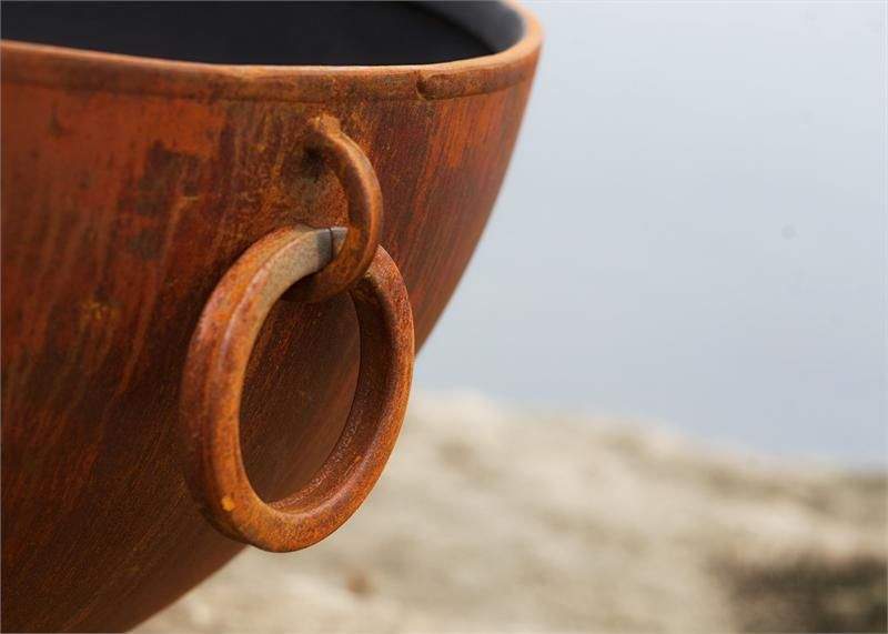 Wood fire pit side loop handle on copper-brown metal bowl, rusted finish.