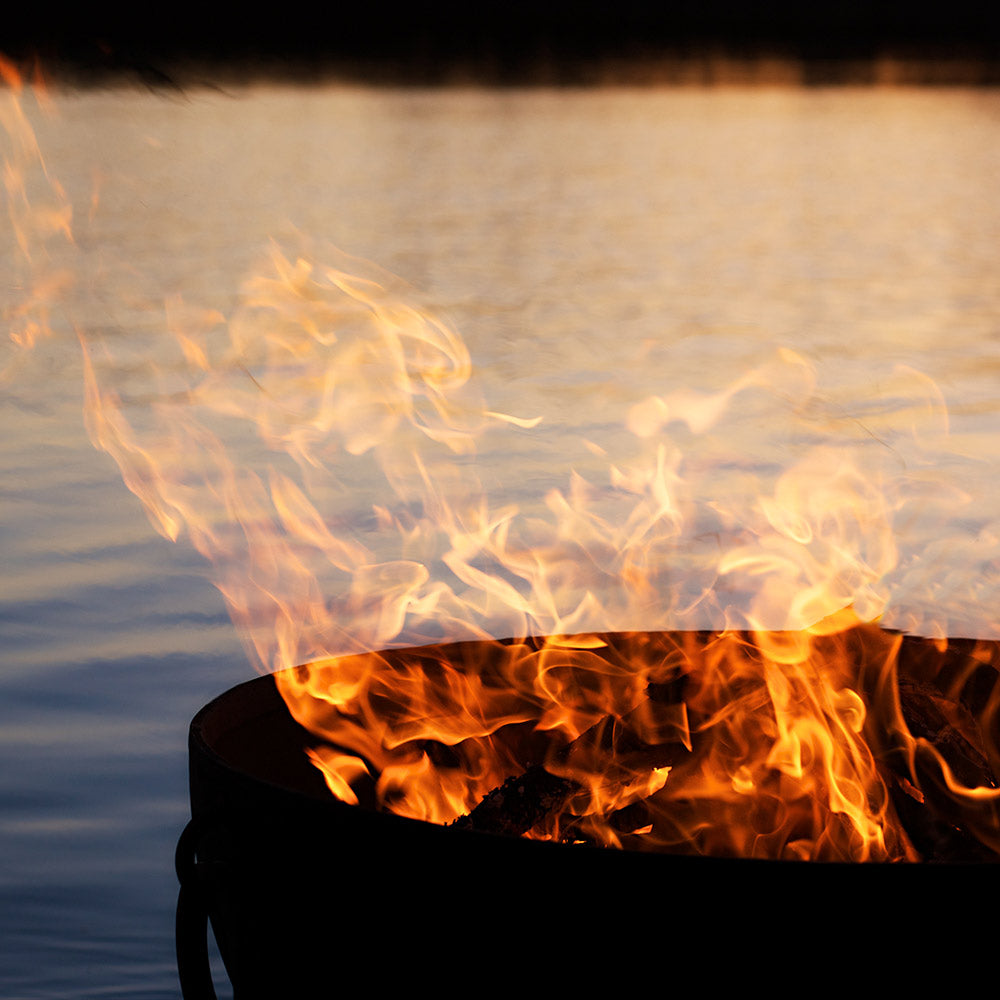 Wood fire pit flames rising from dark bowl, orange and yellow fire glow.