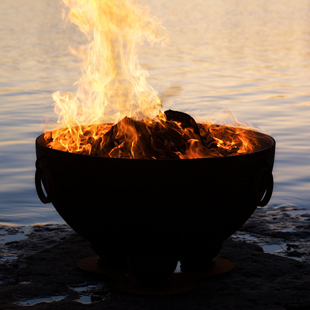Wood fire pit burning logs inside dark metal bowl, flames at top rim.