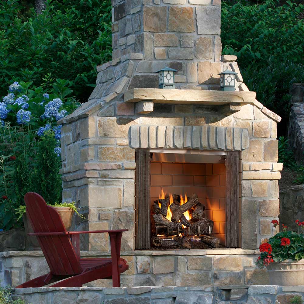 Outdoor stone wood fireplace with open front and burning logs, mantel surround