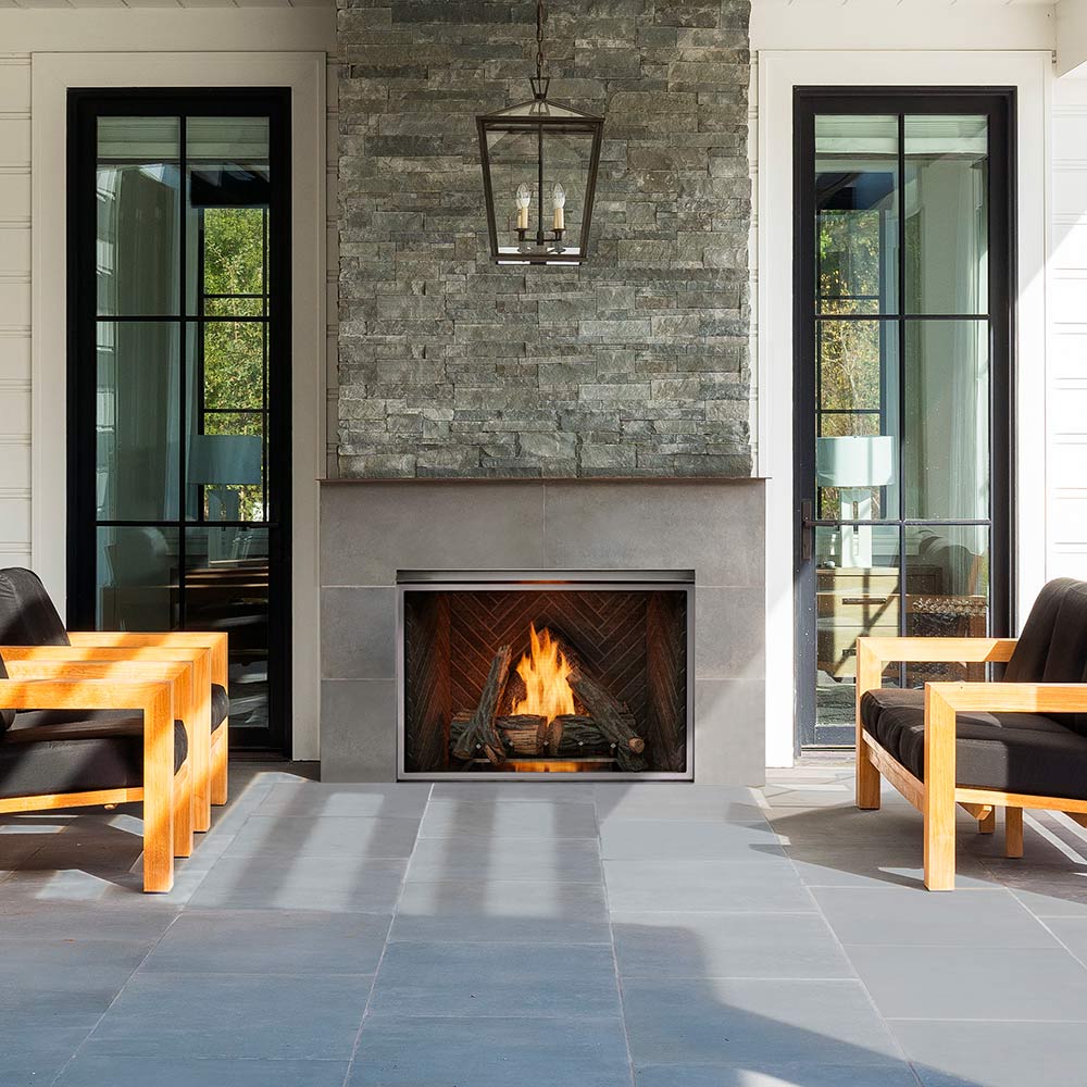 Outdoor gas fireplace built into a stone wall with burning log set