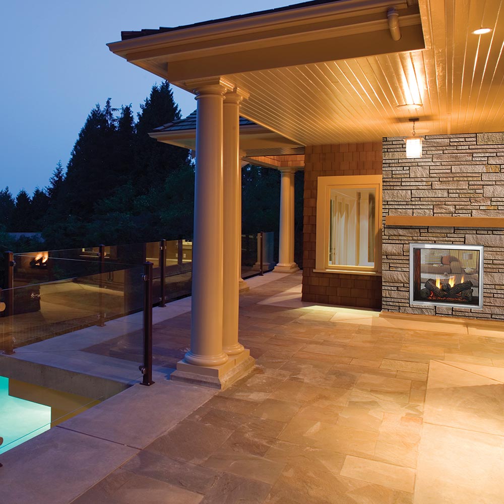 Outdoor see-through gas fireplace set in stone wall with burning fire