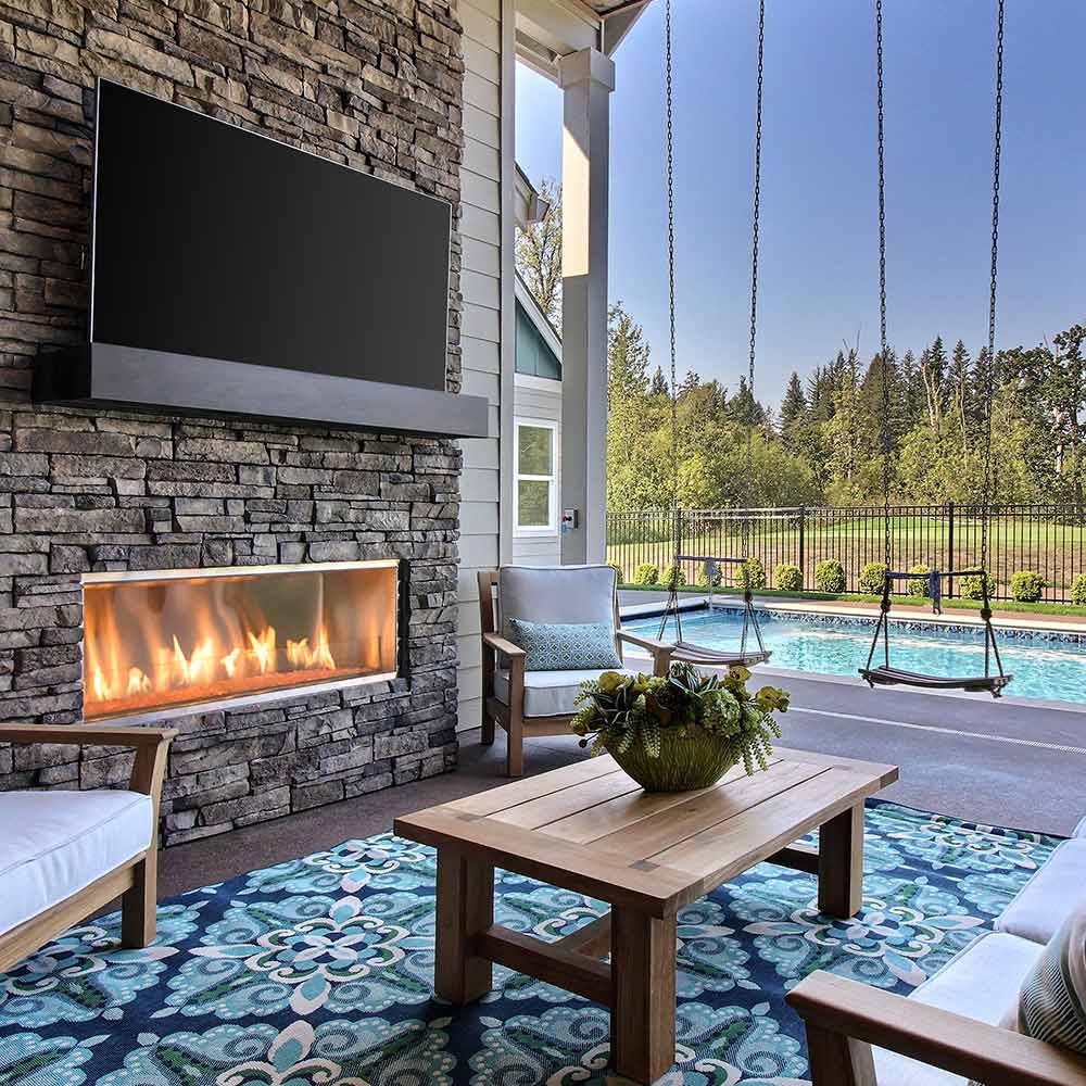 Outdoor linear gas fireplace set in stone wall, glass or metal firebox with flames
