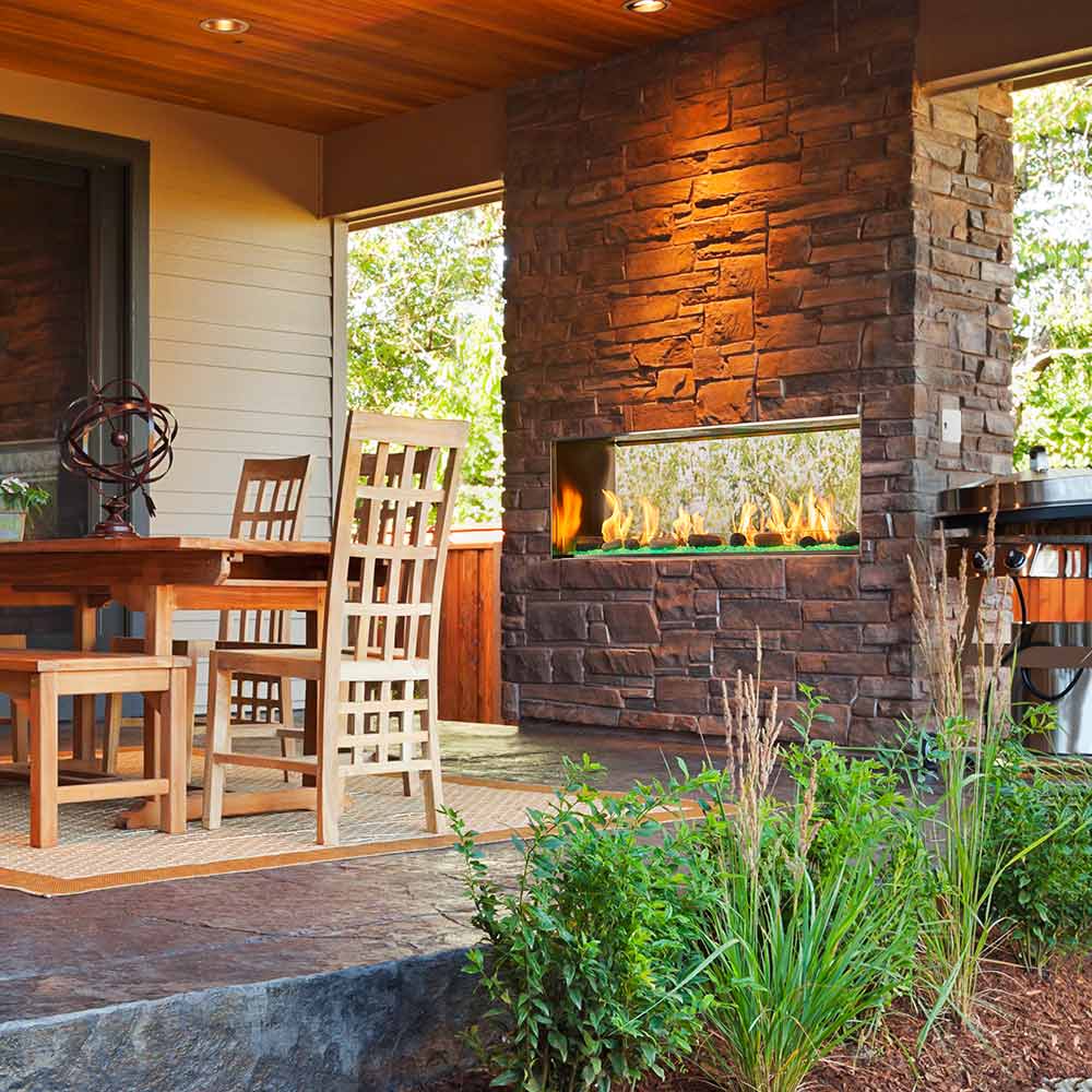 Outdoor stone wall linear gas fireplace with flames visible through glass