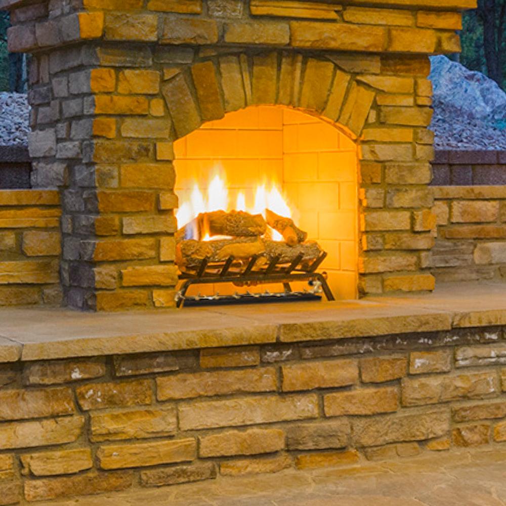Crossfire burner grate inside stone fireplace with tall orange flames