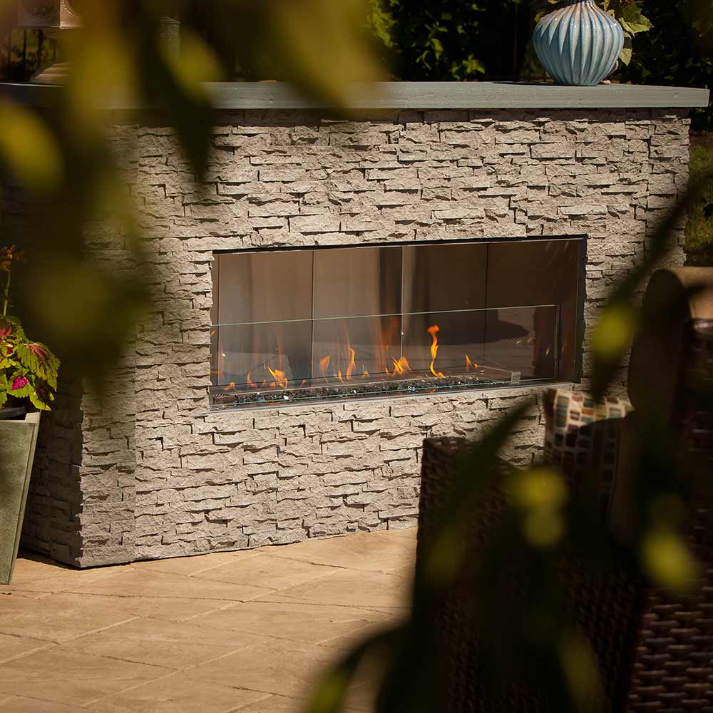 Outdoor linear gas fireplace in stone surround, flames visible through glass window