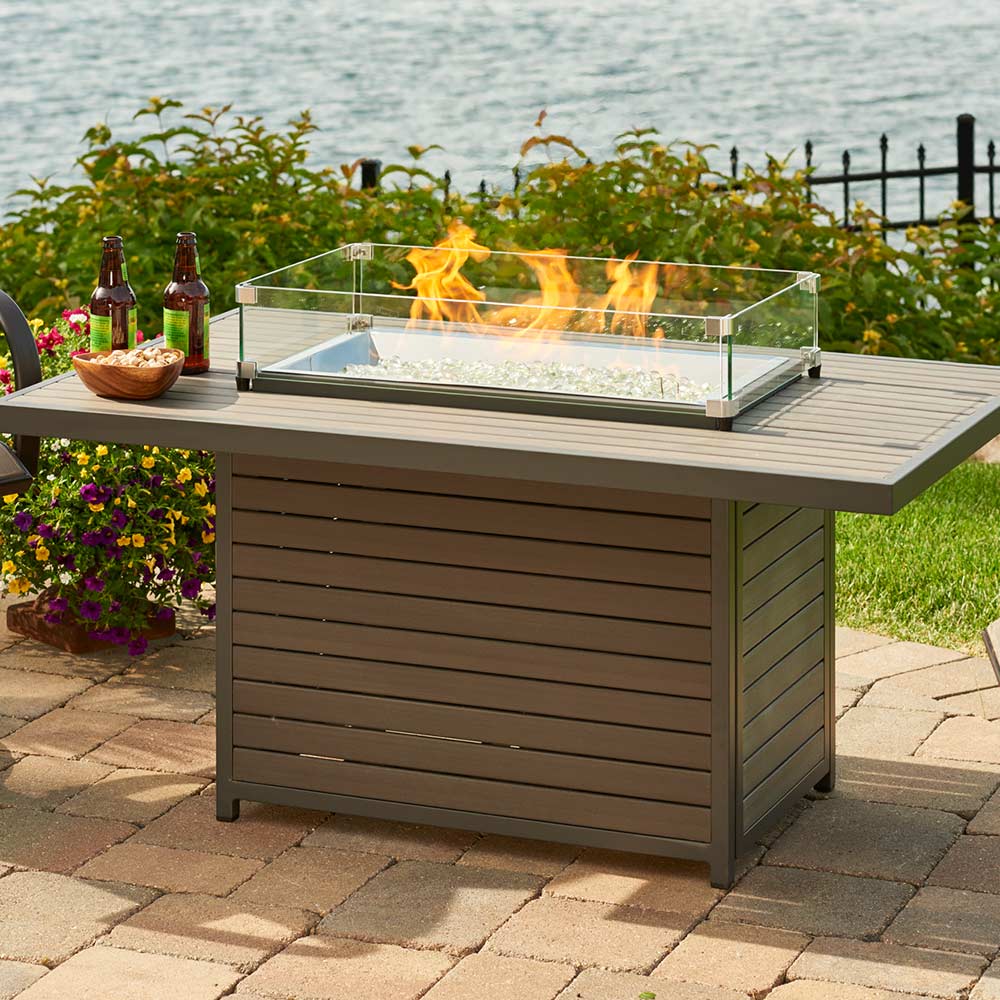 Outdoor fire pit table with flames on a patio by a body of water