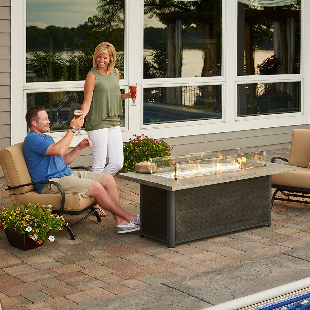 Outdoor gas fire pit table with dark base and gray tabletop, flames visible
