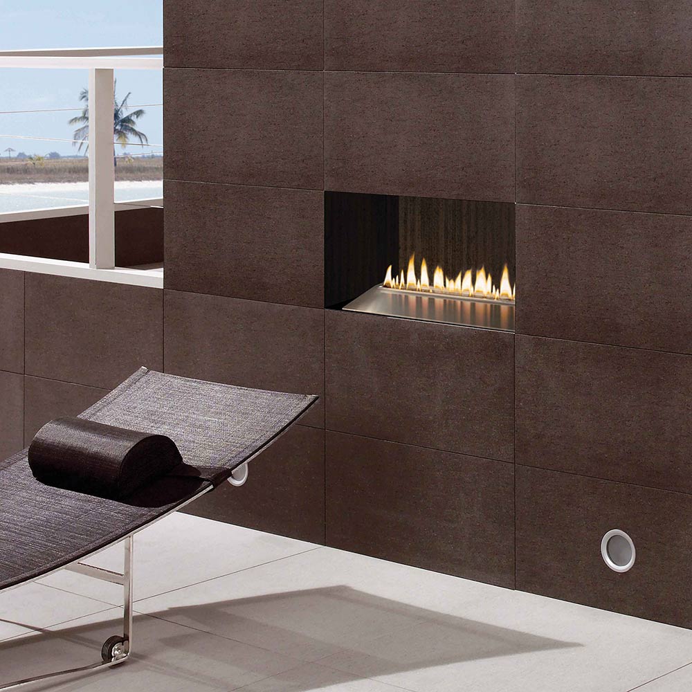 Wall-mounted gas burner in a stone alcove with multiple flames, stainless steel tray