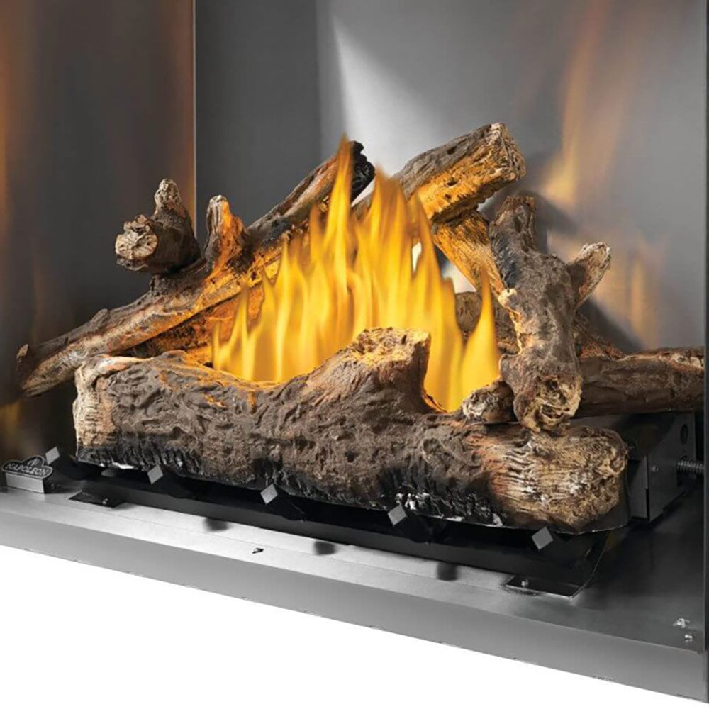 Outdoor gas fireplace log kit with dark logs burning in a metal firebox, orange flames