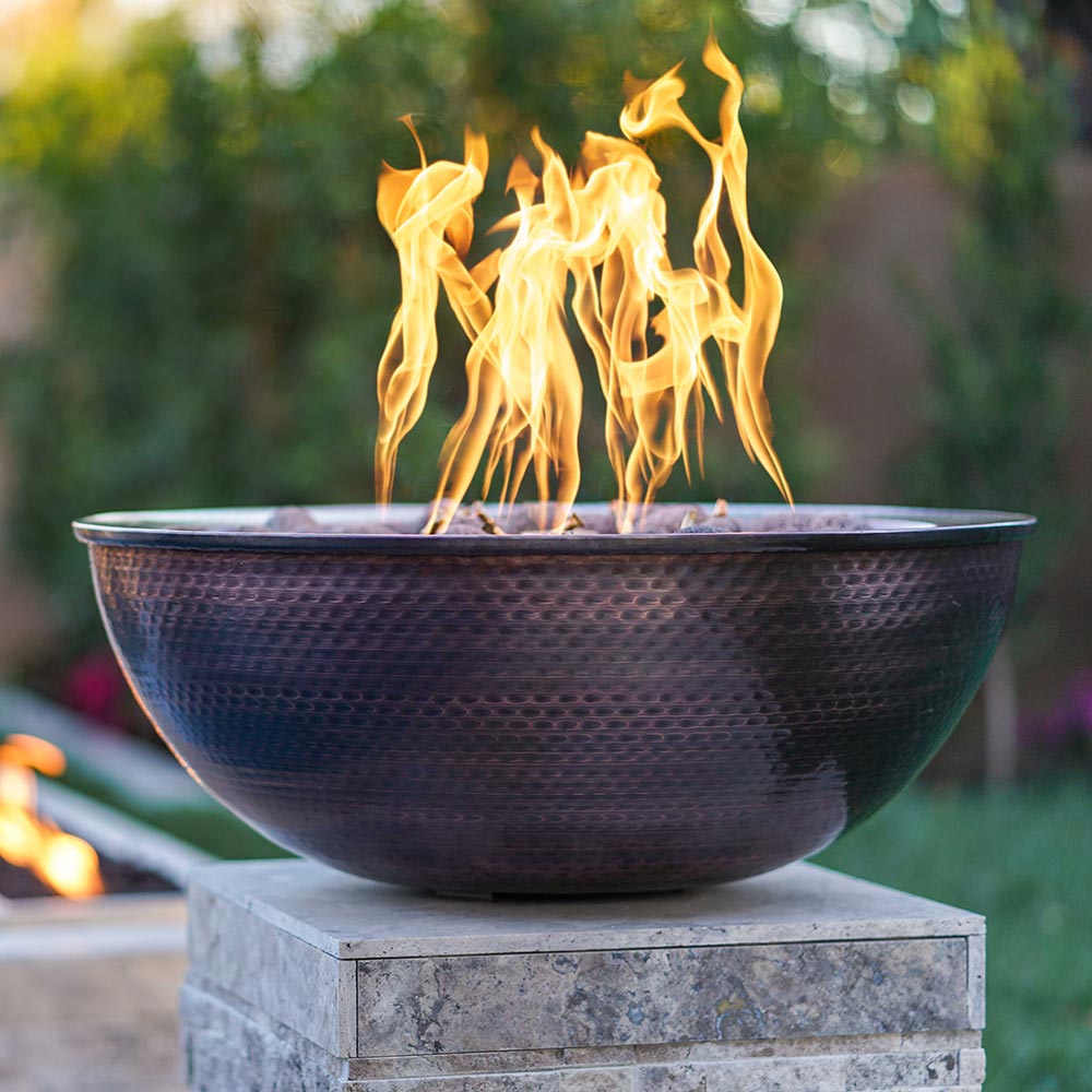 Round copper gas fire bowl with visible flames and dark lava rocks