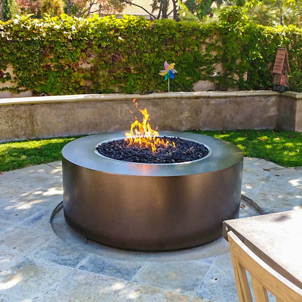 Powder-coated steel gas fire pit with round bowl and visible flames in a backyard setting