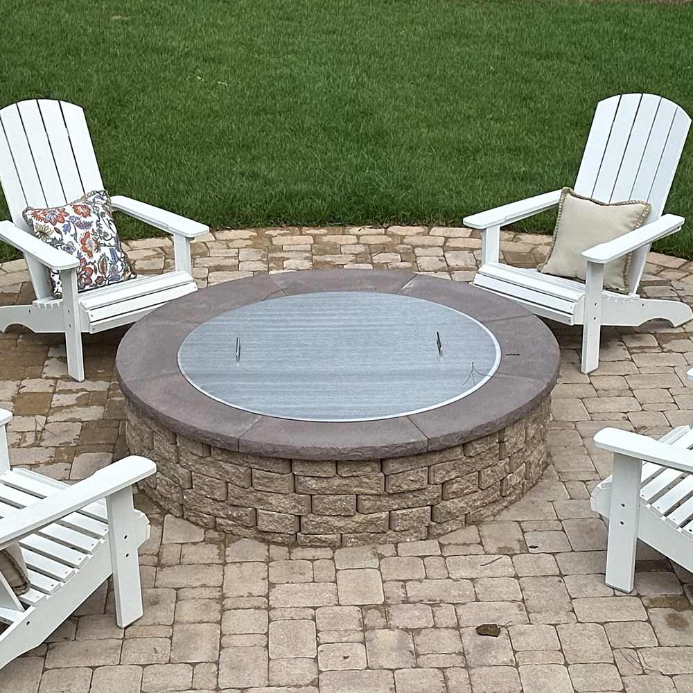 Round fire pit cover on stone fire pit top, brushed stainless steel