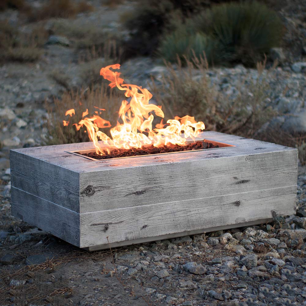 Rectangular wood-grain concrete fire pit with orange flames, dark gray finish on rocky ground