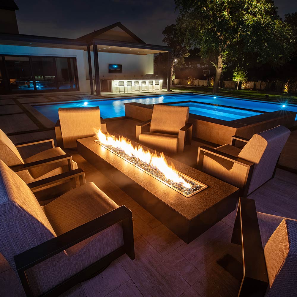 Outdoor dark gray linear gas fire pit with flames in a rectangular burner pan