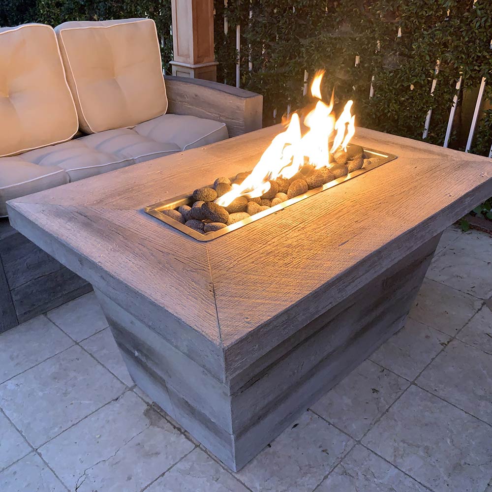 Rectangular wood-grain concrete gas fire pit with flames on outdoor patio