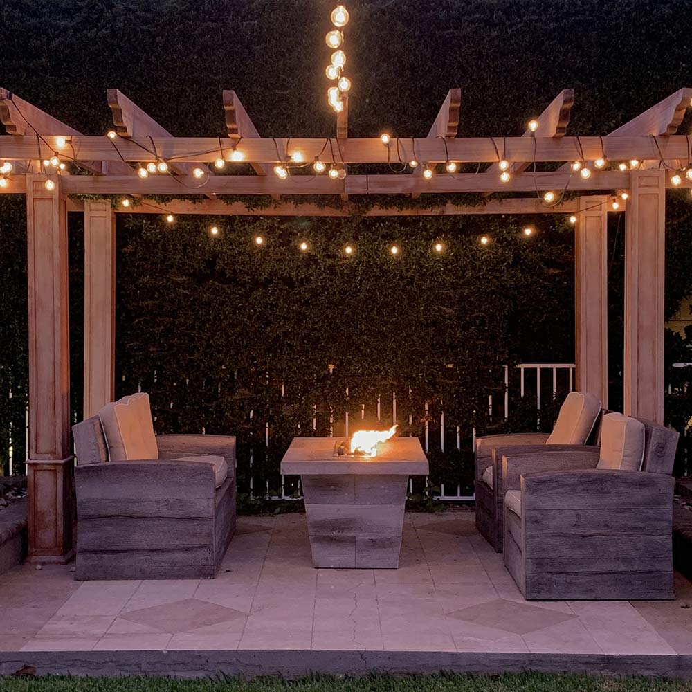 Rectangular wood-grain concrete gas fire pit with flames in outdoor seating area