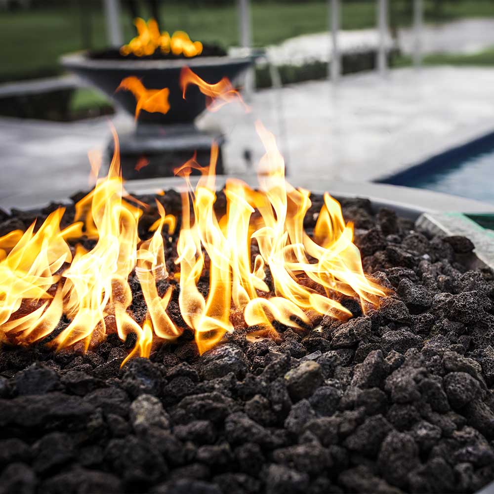 Flames burning in a round concrete gas fire bowl over dark lava rocks