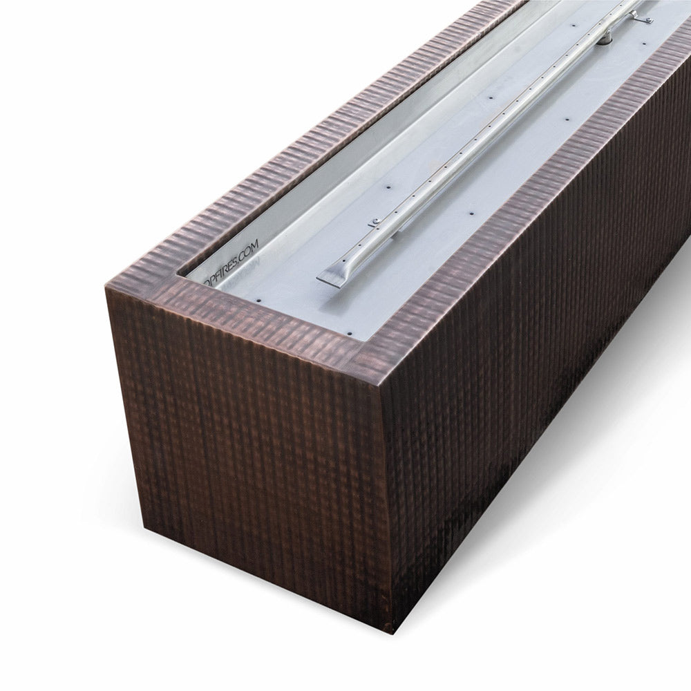 Linear gas fire pit showing burner tray and burner components in dark copper-toned housing