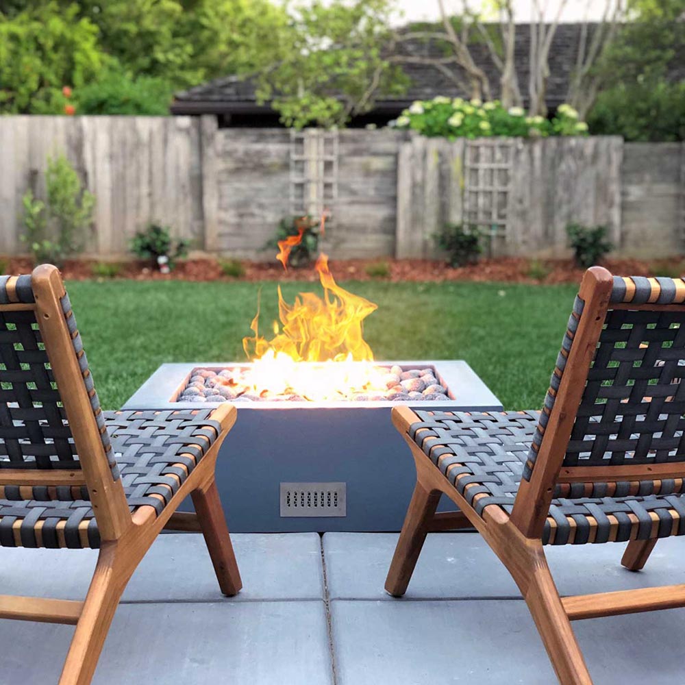 Square concrete gas fire pit with open flame burning in the center