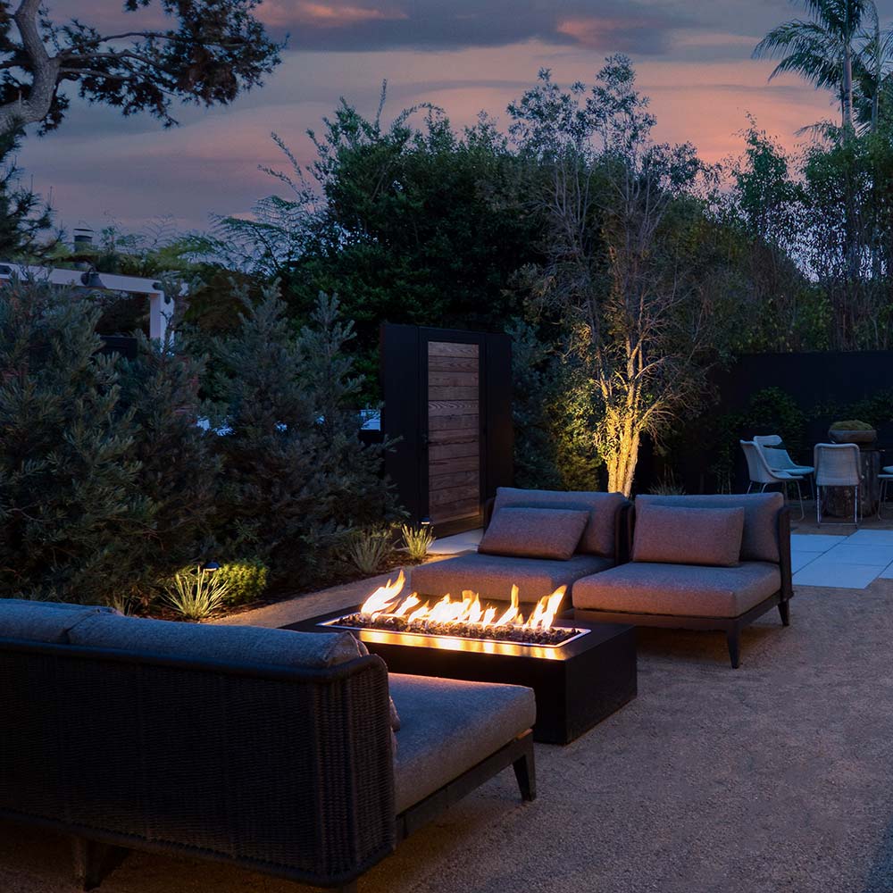 Outdoor seating set with rectangular linear gas fire pit burning at dusk