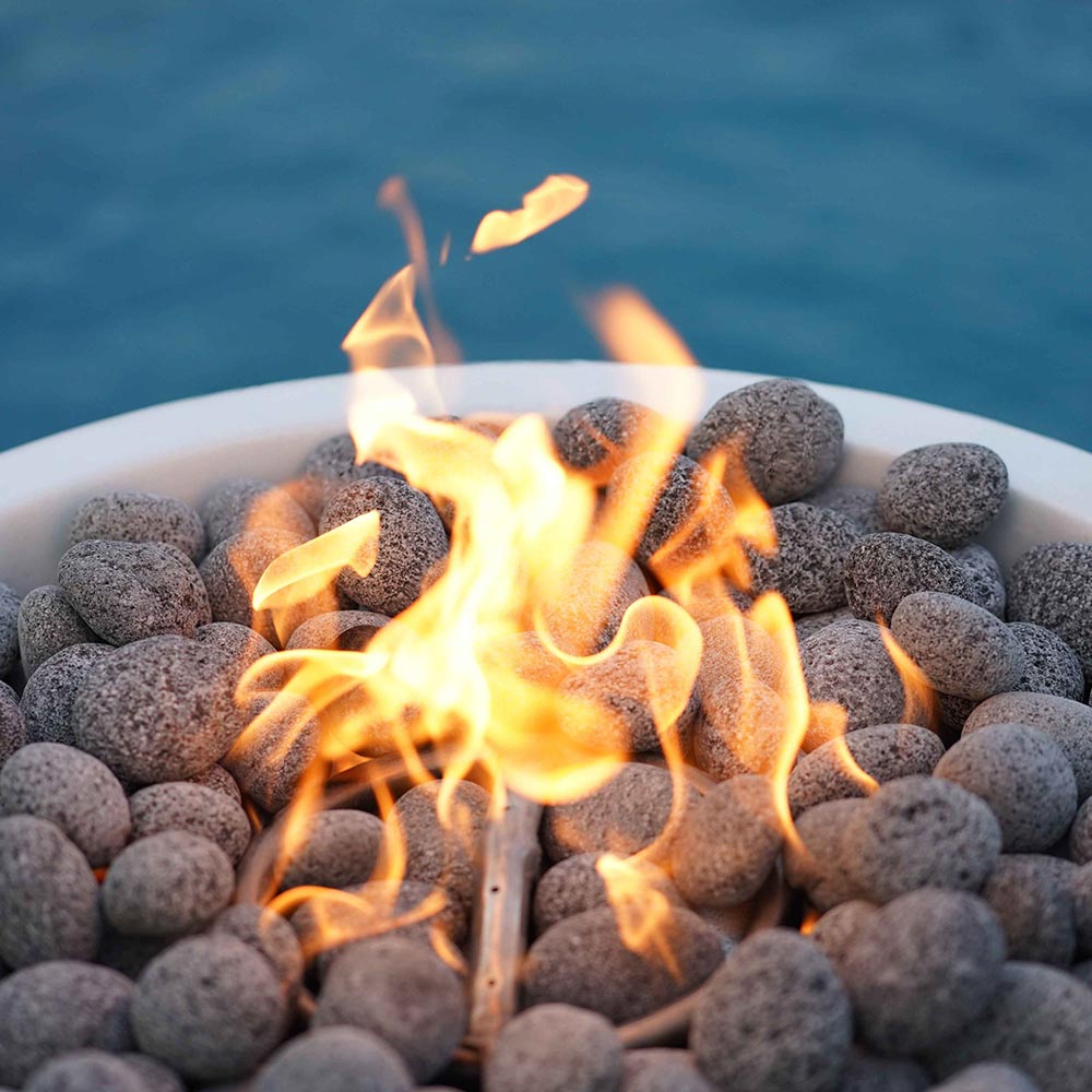 Round concrete gas fire pit with flame on gray lava rocks.