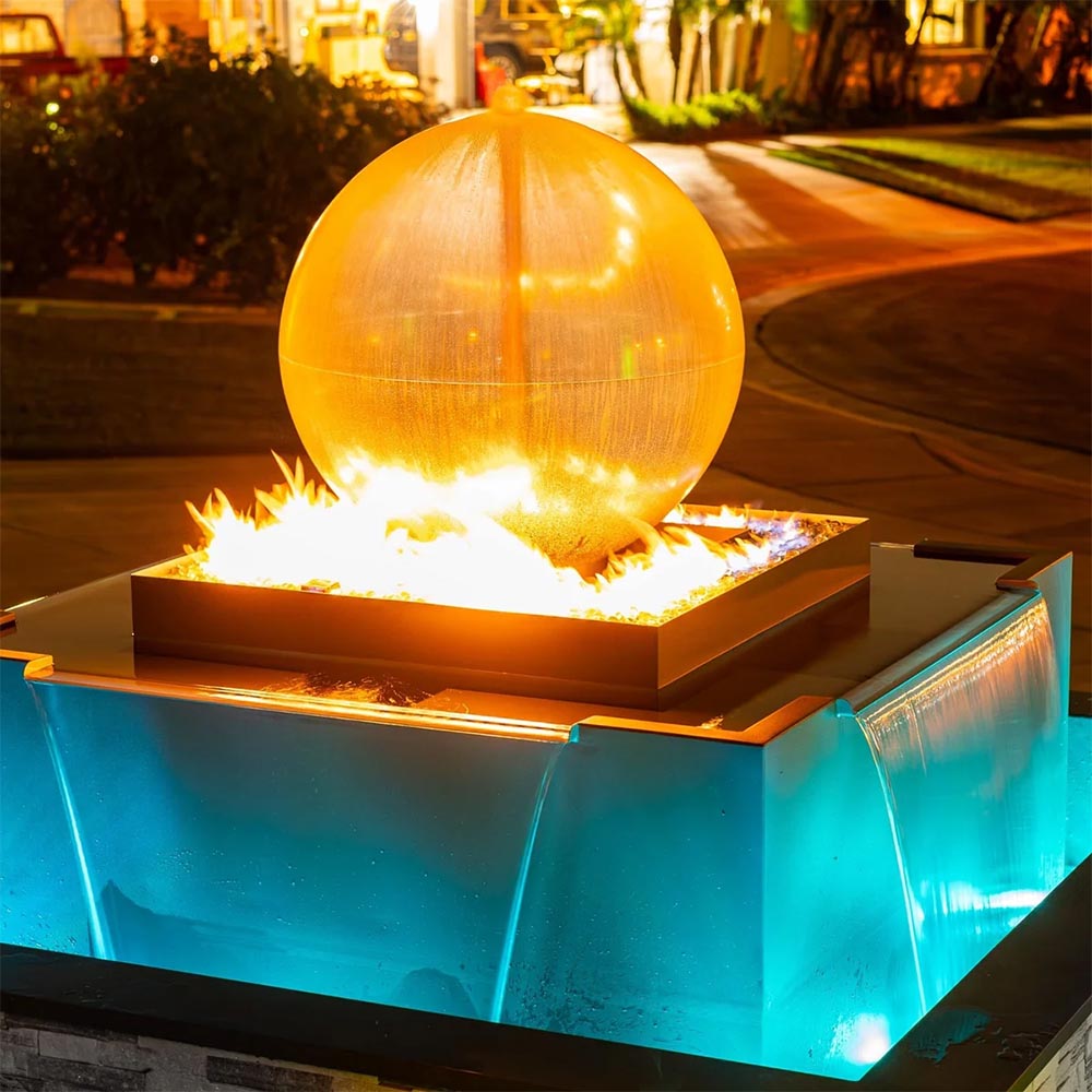 Outdoor gas fire and water bowl with glowing flames and lit blue pool under silver sphere