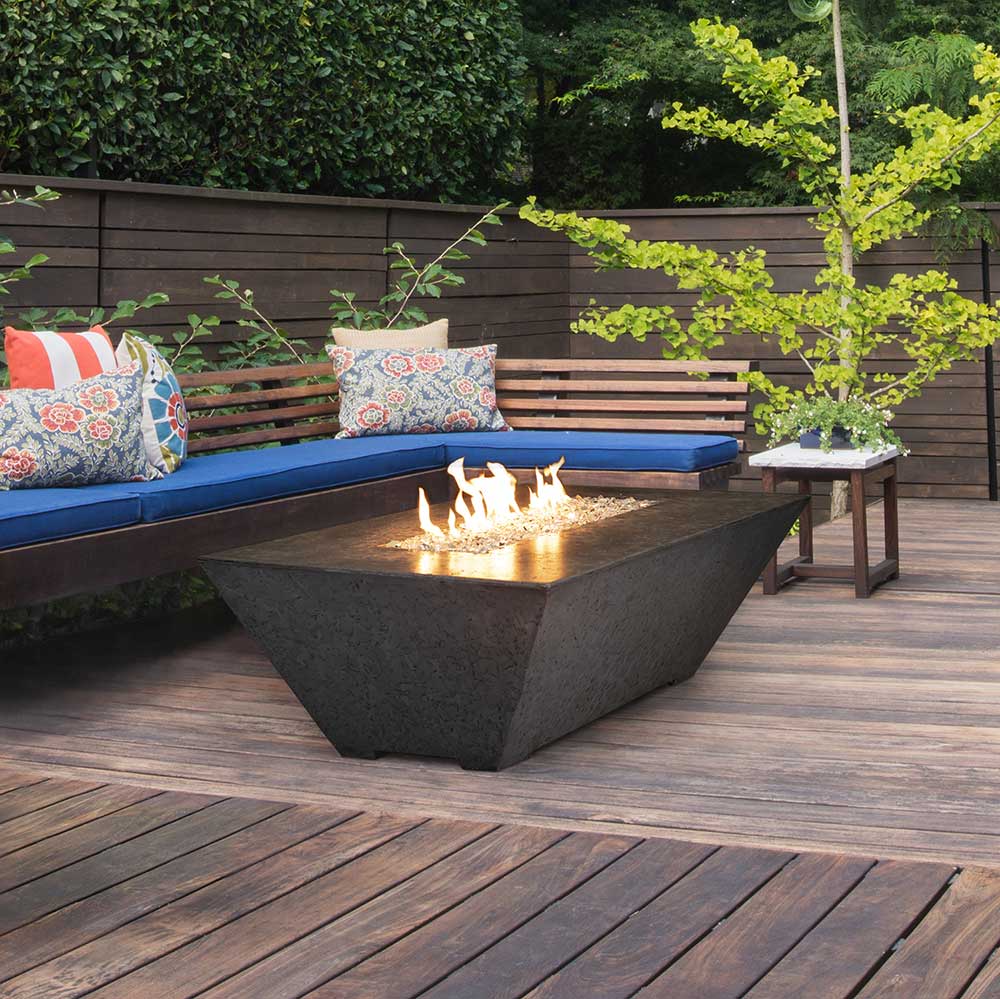 Rectangular concrete gas fire pit with lit flames, dark gray finish on outdoor deck